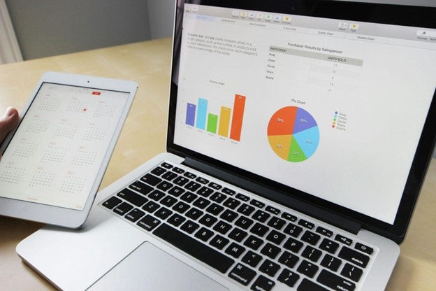 A laptop displaying graphs and a tablet with a spreadsheet on a desk.