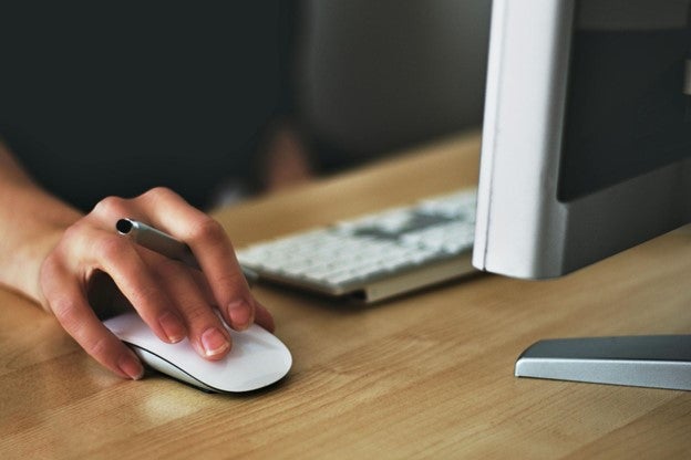 Person's hand using a white computer mouse on a desk next to a keyboard.