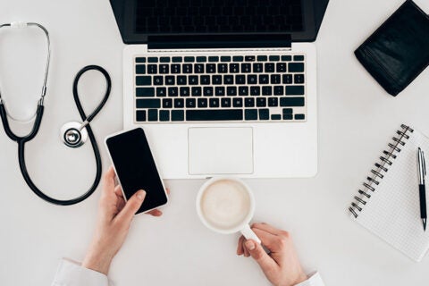 partial view of doctor at workplace with laptop