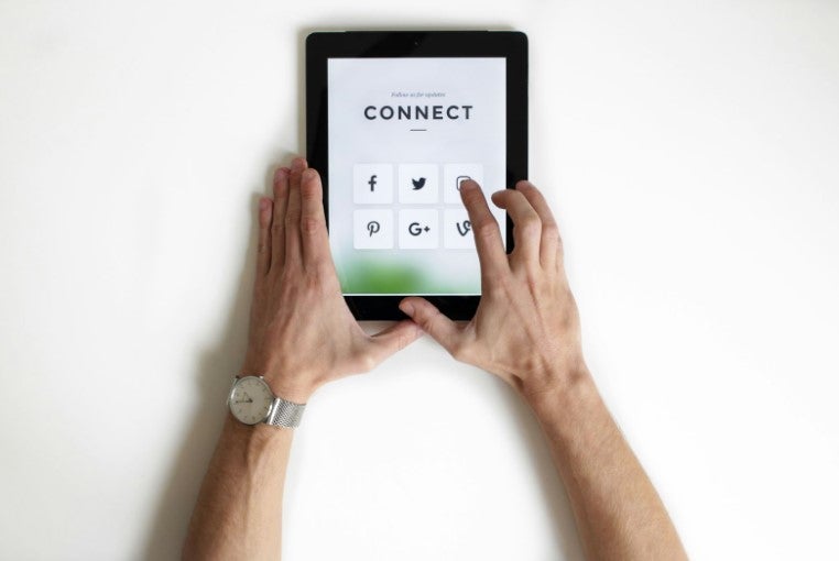 Hands holding a tablet showing social media icons with the word "CONNECT" on screen.