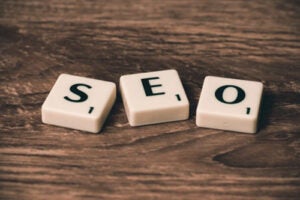 Three tiles with letters spelling "SEO" on a wooden surface.