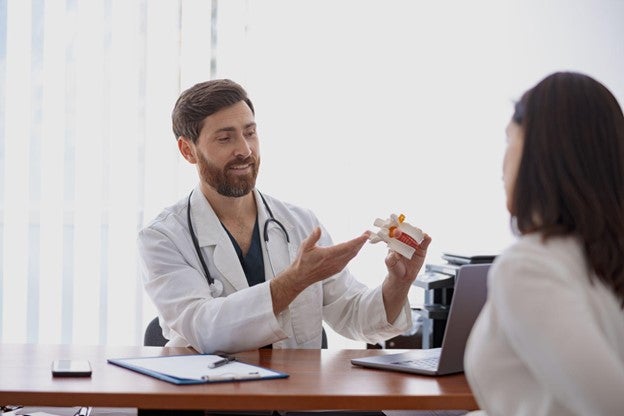A doctor in a white coat discussing medication with a patient at a desk.