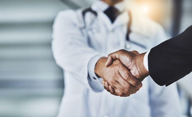 Close-up of a handshake between a person in a white lab coat and another person, blurred office background.