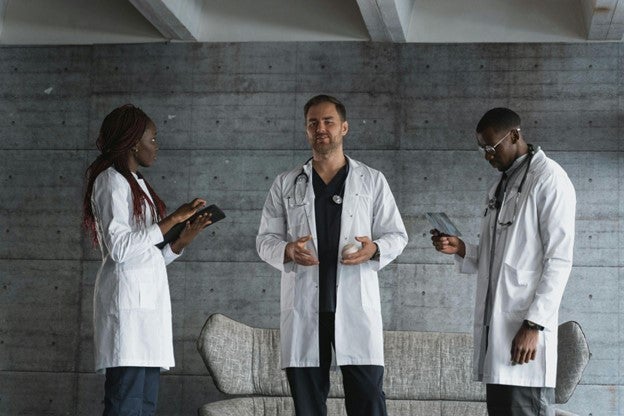 Three medical professionals in white coats having a discussion in a modern lounge area.
