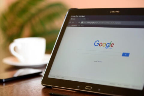 Samsung tablet displaying Google search homepage, with a coffee cup and stylus in the background.