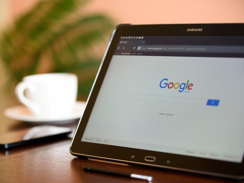 Samsung tablet displaying Google search homepage, with a coffee cup and stylus in the background.